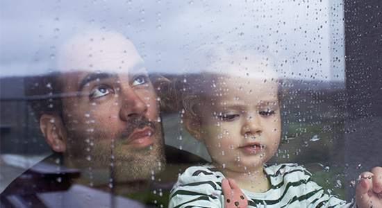 Man and young child looking out a rainy window