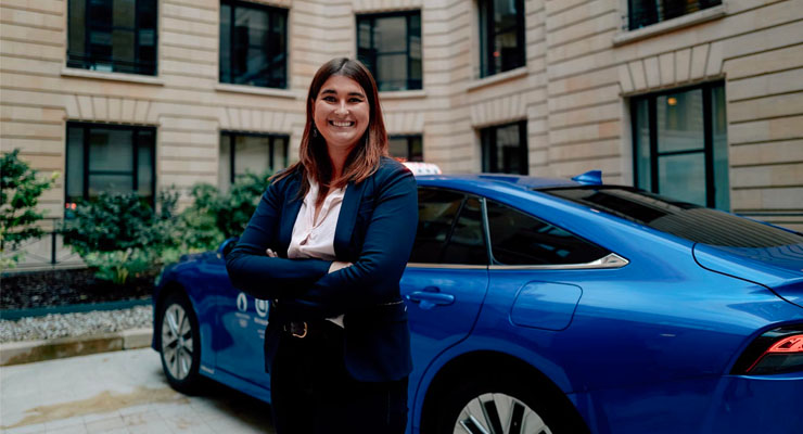 A smiling woman stands next to a taxi