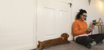 Smiling woman looking at her phone sits on the floor next to a door that has a woolly door stop in the shape of a dog.