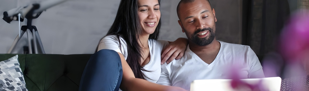 A happy couple sitting on their couch viewing their laptop screen