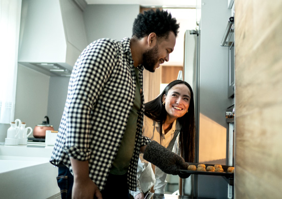 A happy couple carefully removing food from the oven.